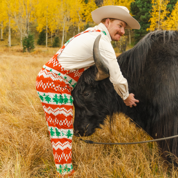 Cowboy in a white hat and holiday fair-isle Shinesty pajamaralls patting a yak in a golden aspen meadow