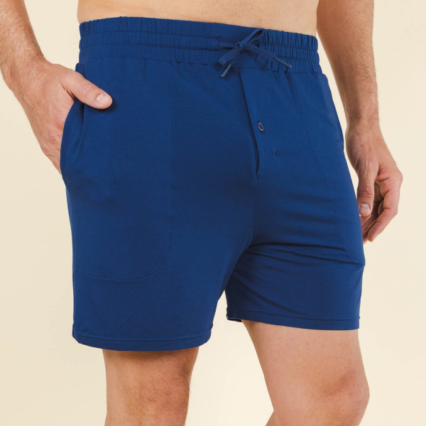 Tied drawcord and button fly on navy MicroModal pajama shorts, one hand pocketed against a cream wall