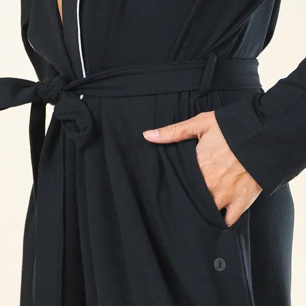 Hand resting in the pocket of a black Shinesty robe, self-fabric belt knotted at the waist