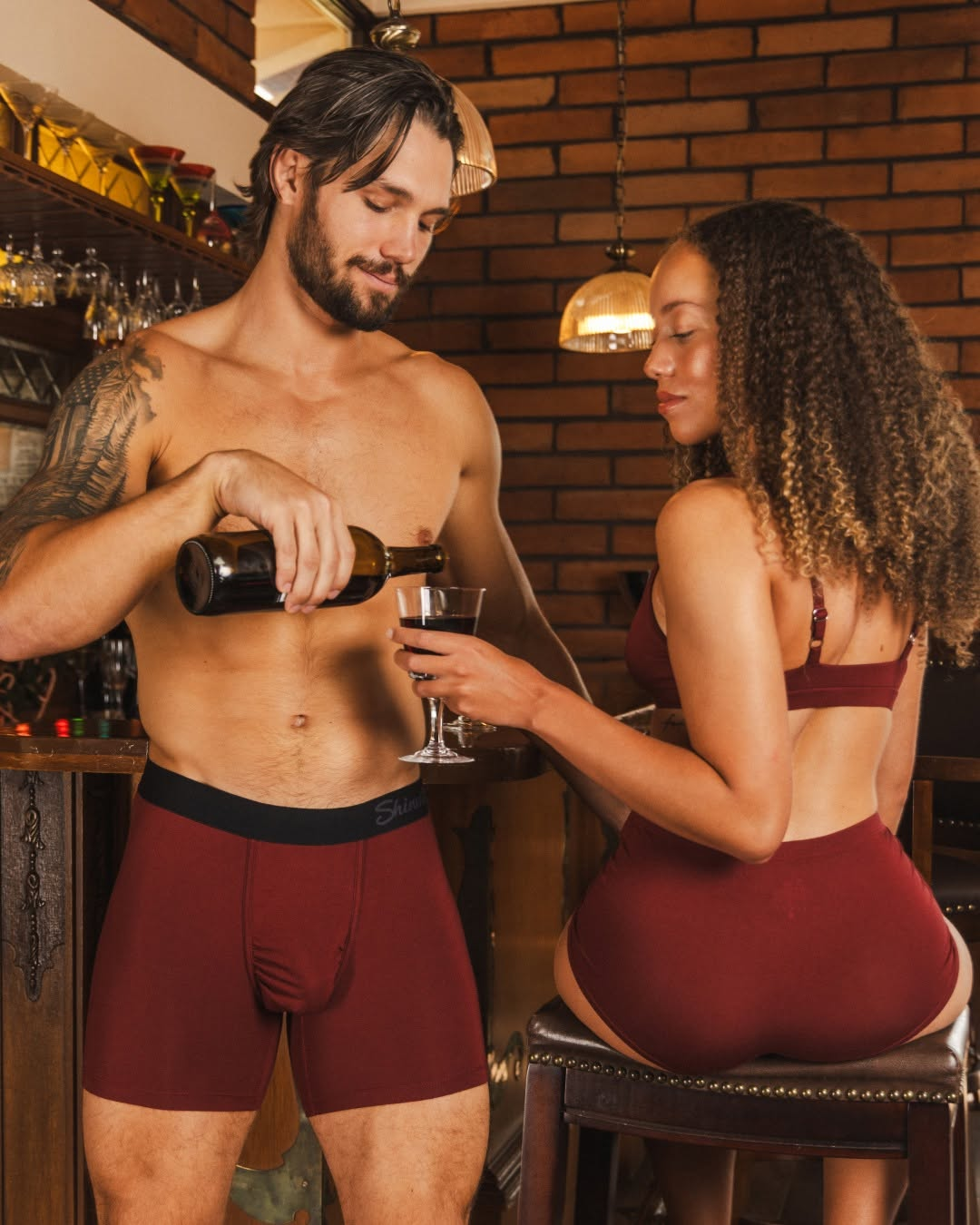 Couple in matching burgundy underwear pouring a drink at a bar